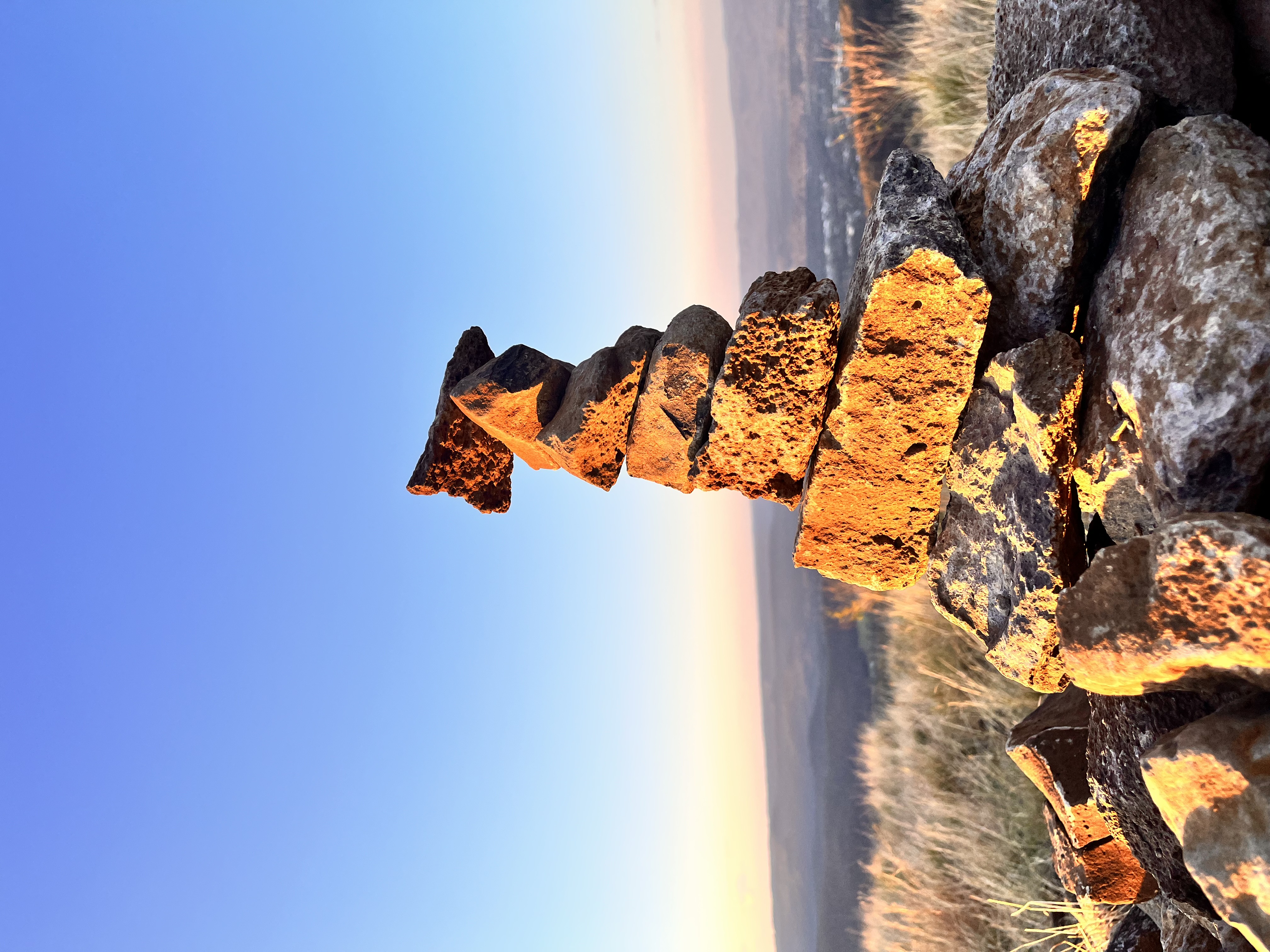 A stack of stones lit by golden sunlight beneath a clear blue sky
